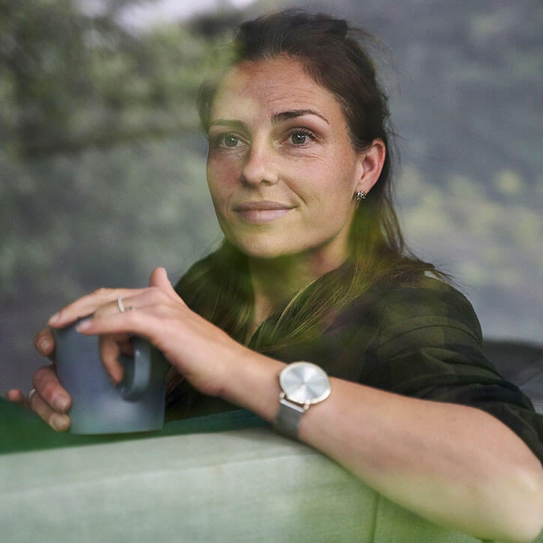 Nachdenkliche Frau hält Kaffeetasse beim entspannen auf der Couch in der Hand und schaut aus dem Fenster