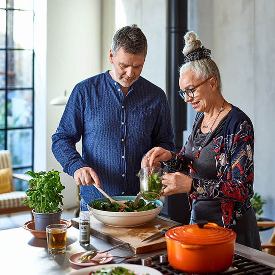 Erwachsener Mann und ältere Frau stehen in der Küche und machen Mittagessen