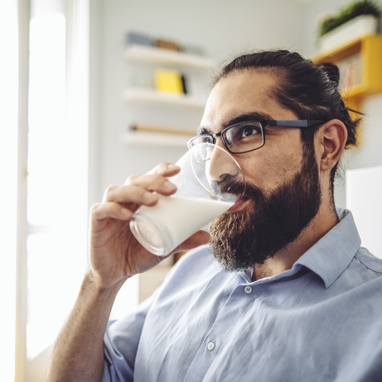 Bärtiger Mann mit Brille trinkt ein Glas Milch