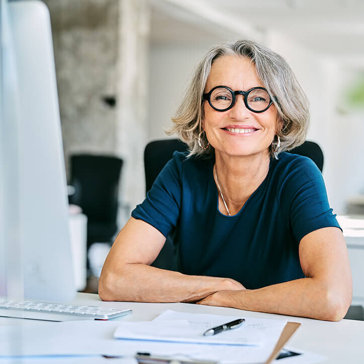 Lächelnde Geschäftsfrau am Schreibtisch im Büro | Doppelherz