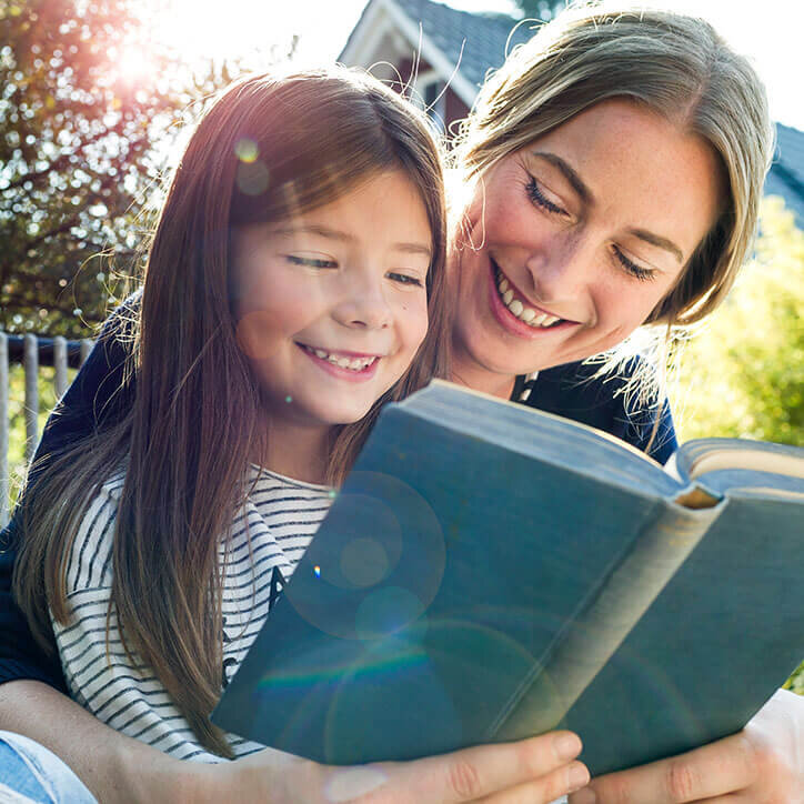 Mutter liest im Garten ein Buch mit ihrer Tochter | Doppelherz