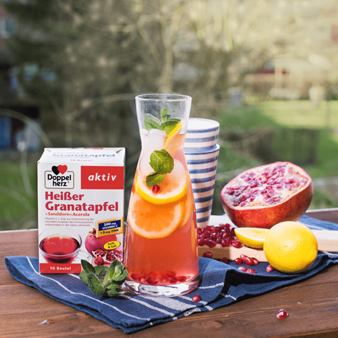 Doppelherz Heißer Granatapfel auf einem Gartentisch neben einer Karaffe mit Limonade und aufgeschnittenen Granatäpfeln